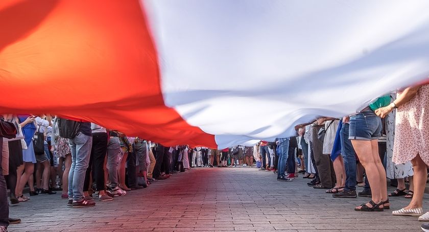 Ludzie trzymający rozciągniętą flagę Polski
